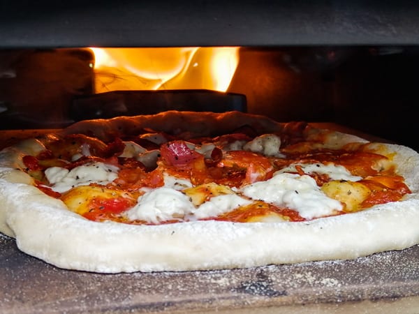 The flames heat the air above the pizza to a higher temperature than the stone