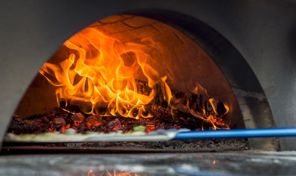 Neapolitan pizza being loaded into large wood fired oven