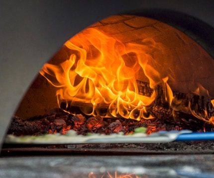 Neapolitan pizza being loaded into large wood fired oven